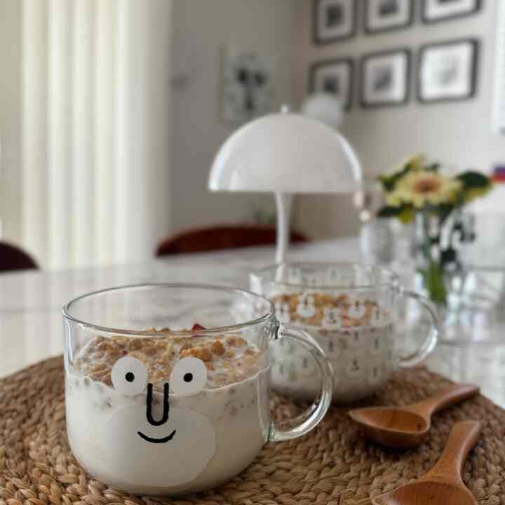 ナチュラルな雰囲気のキッチン空間、ガラスのシリアルカップと白いテーブルランプが配置された印象的な食事スペース