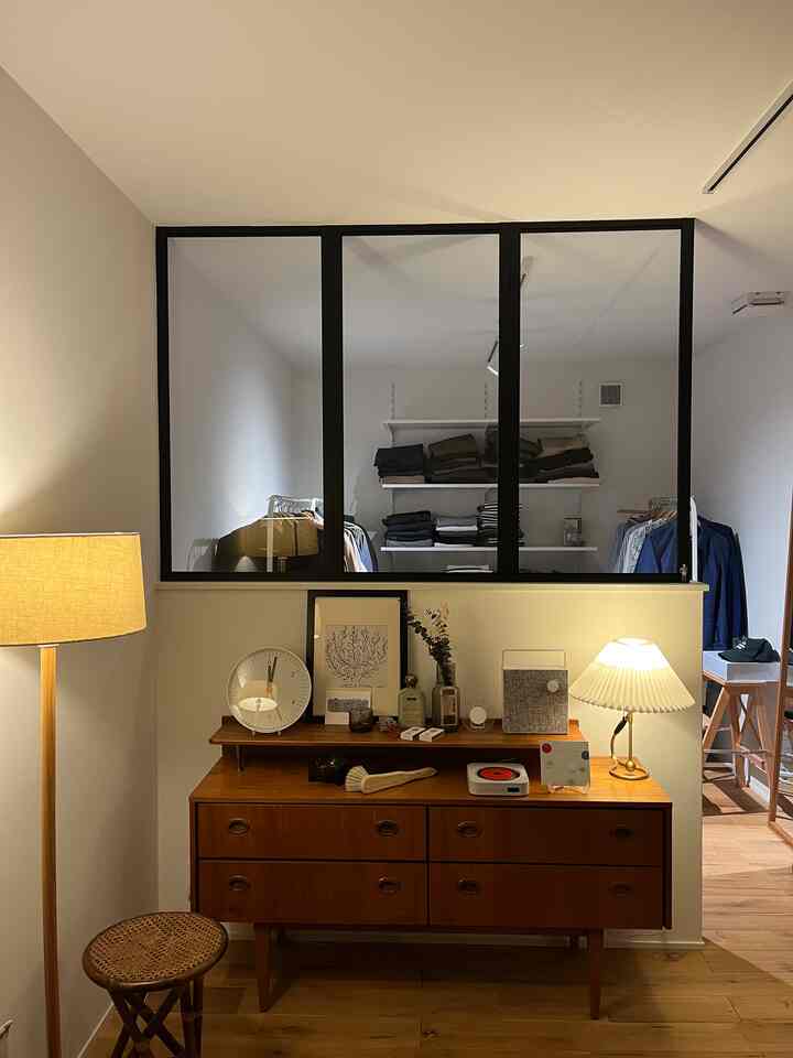 Wood tone floor and medium wooden dresser beneath a white wall featuring an interior window revealing a walk-in closet