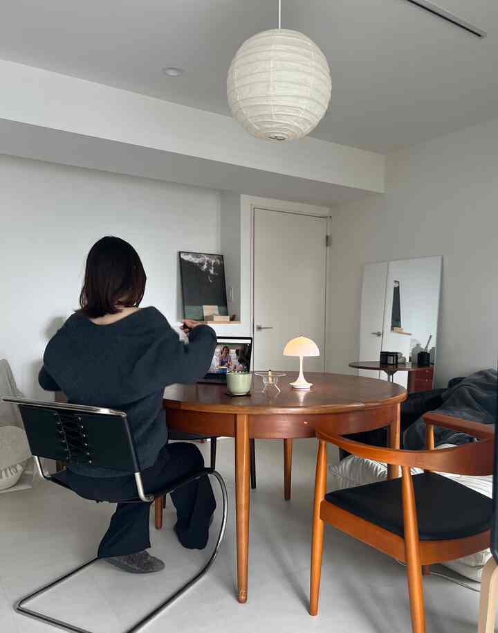 White-walled and ceiling living space featuring a mid-century modern round wooden dining table with varied chairs, creating a warm atmosphere