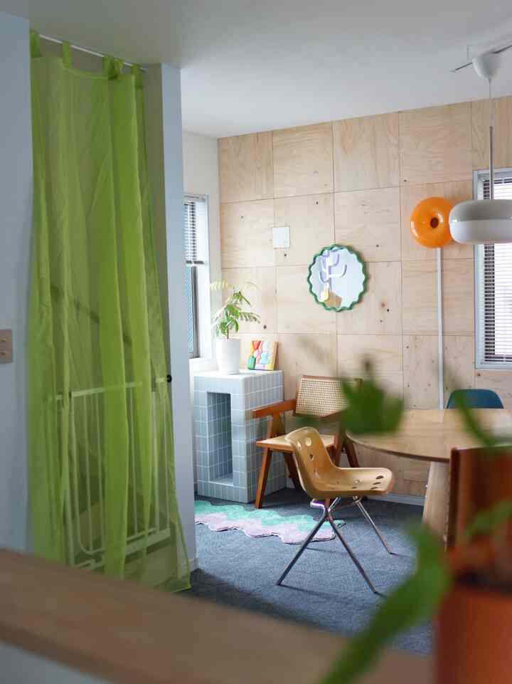 Cozy dining room interior featuring light green sheer curtains by stairs, light wood panel walls, dining table and chairs