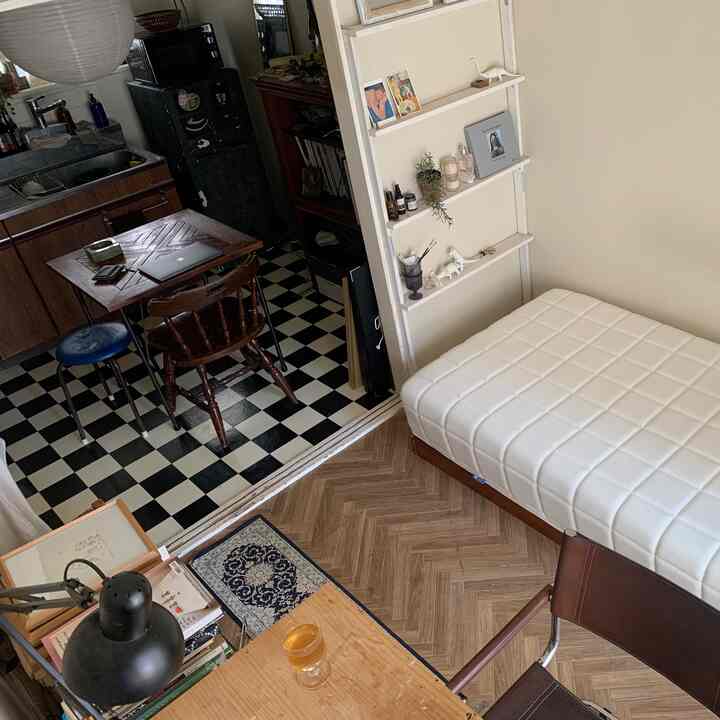 Beige-toned studio apartment featuring a white mattress bed and compact dining table with natural wood furniture creating a cozy atmosphere