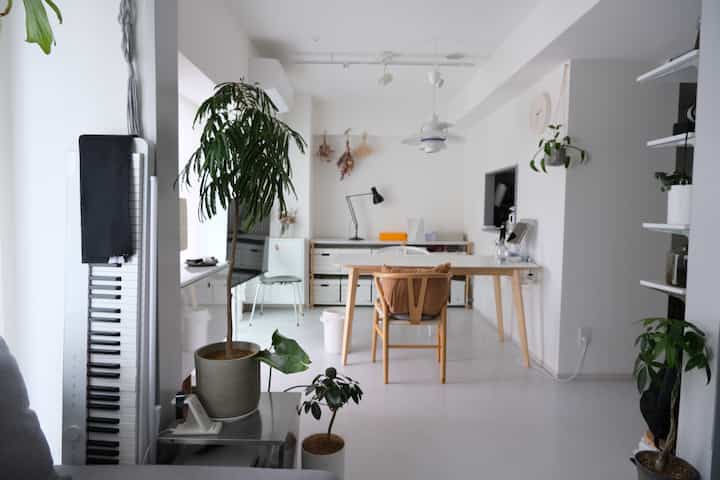 白を基調としたダイニングルームとホームオフィス、自然な植物とシンプルなダイニングセットが配置された明るく清潔感のあるインテリア