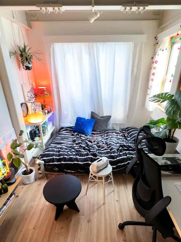 Bright white walls and wood tone flooring in a compact studio featuring a black striped bed and ergonomic office chair