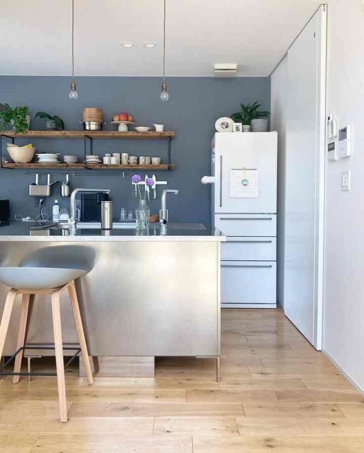 Blue accent wall and white refrigerator with stainless steel kitchen island and wooden stool in a simple modern kitchen space