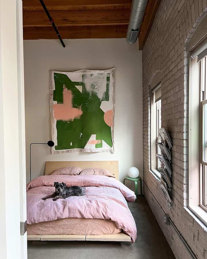 Natural-toned bedroom with pink bedding featuring green abstract wall art and a pet dog creating a cozy atmosphere