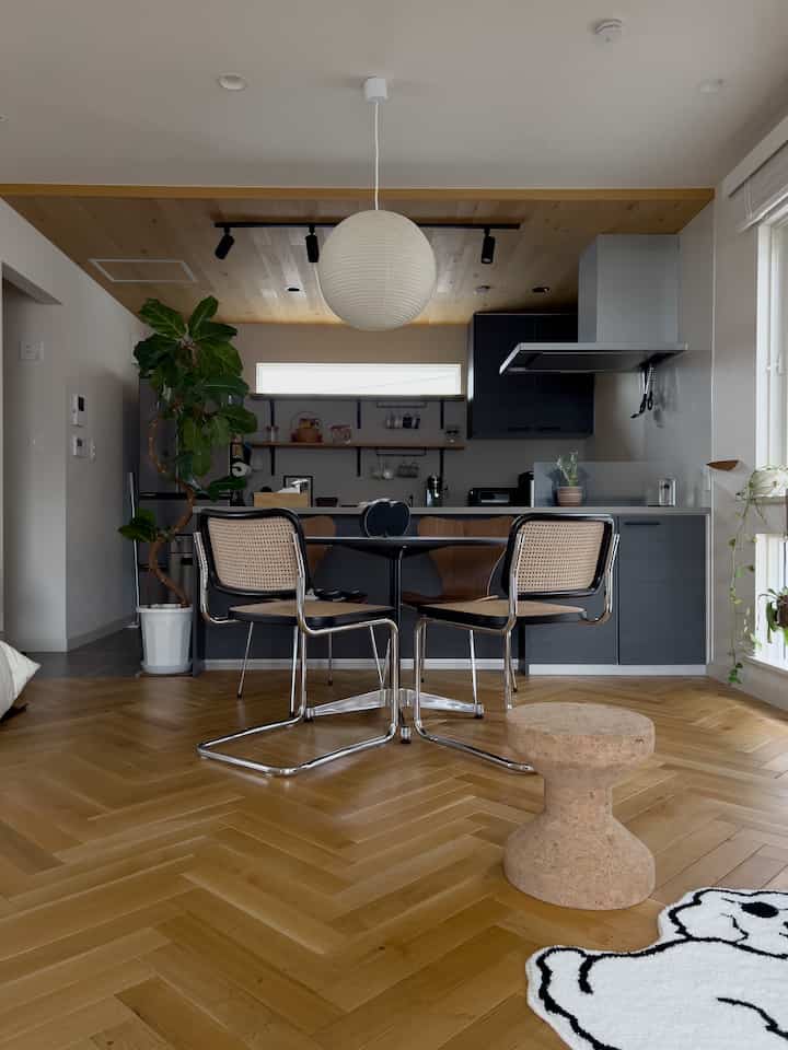 木目調の床と天井が調和するモダンなキッチンとダイニングルーム、ペンダントライトとコルクスツールが配置された落ち着いた空間