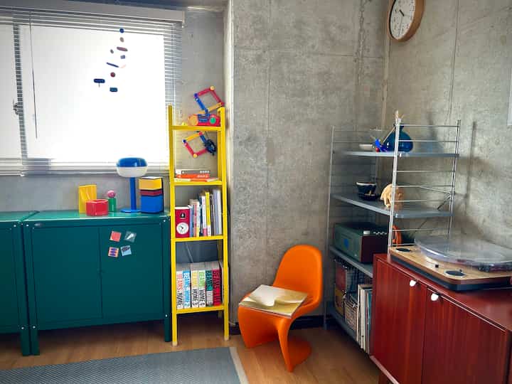 Small Nordic-style study space featuring bright colors, an orange Panton chair, yellow shelving, and a record player creating a cozy atmosphere