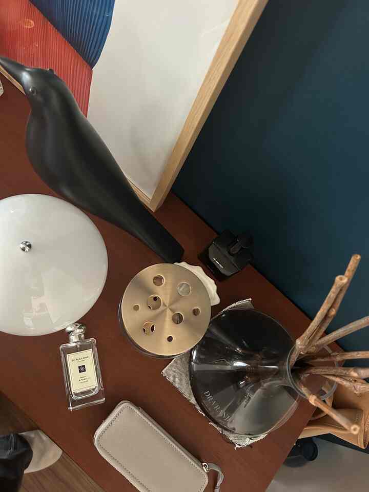 ネイビーの壁とブラウンの木製化粧台にテーブルランプ、花瓶、ディフューザーが置かれた落ち着いたインテリア