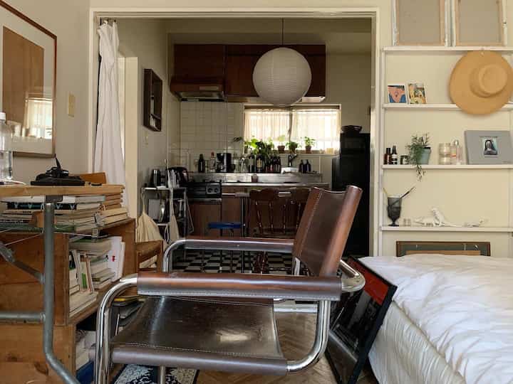 ブラウンとホワイトが調和した小さな一人暮らし用のリビング兼キッチン空間、自然な雰囲気のブラウンのアームチェアと本棚が配置されている印象的なインテリア