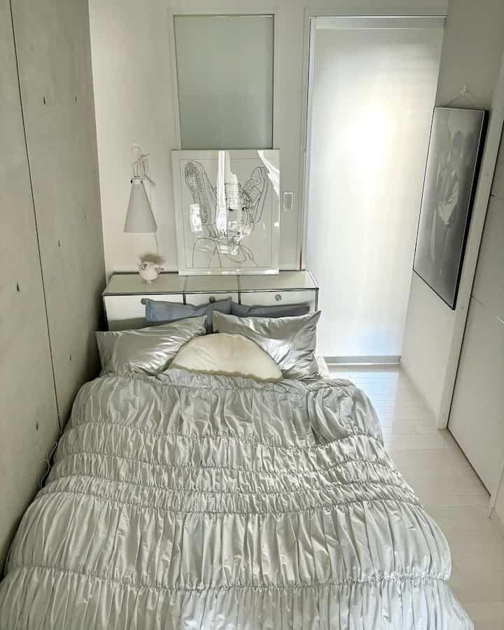 白とシルバーのトーンの寝室、中央に整ったベッドと枕が配置されたシンプルでモダンな印象的な空間