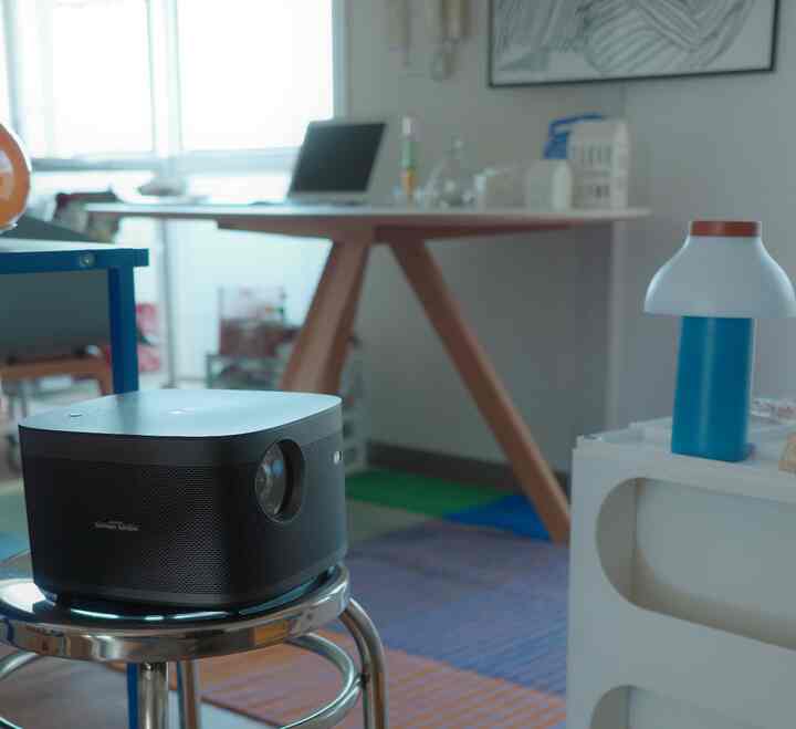 Natural modern home office space in white and wood tones, featuring a projector on a metal stool in the center and a minimalist lamp for a tidy interior