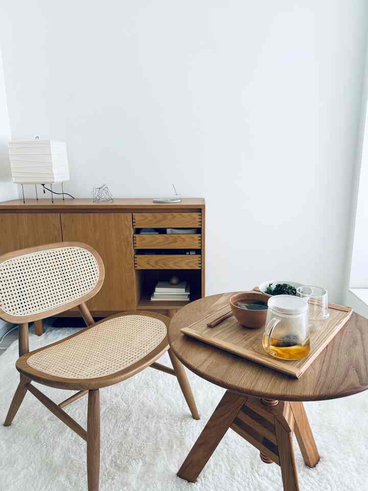 白い壁とカーペットの上に木目調のラウンジチェアと丸いサイドテーブルが配置されたナチュラルな印象のリビング