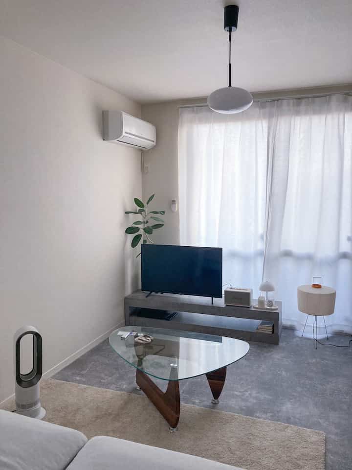 モノトーンとホワイトのトーンでまとめられた一人暮らしのリビング、シンプルで無機質なテレビ台とガラスのコーヒーテーブルが配置された空間