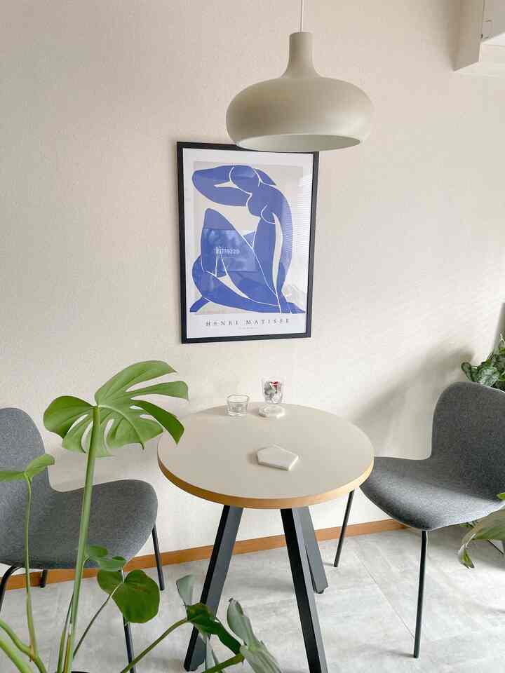 Gray and white toned dining room featuring a round dining table with gray chairs, green plants, and a blue art poster for a clean atmosphere