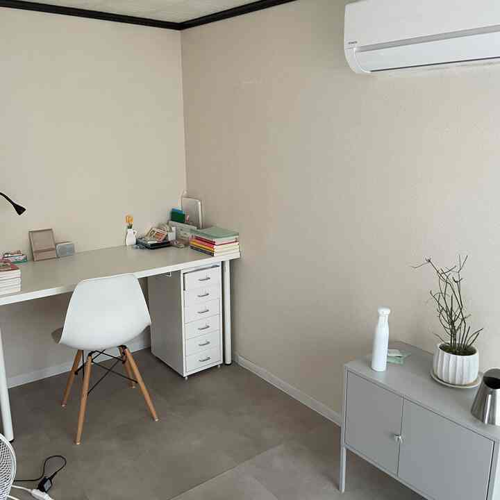 白とベージュのトーンの小さいワークスペース、白い机と椅子、整理されたチェストが配置された印象的な空間