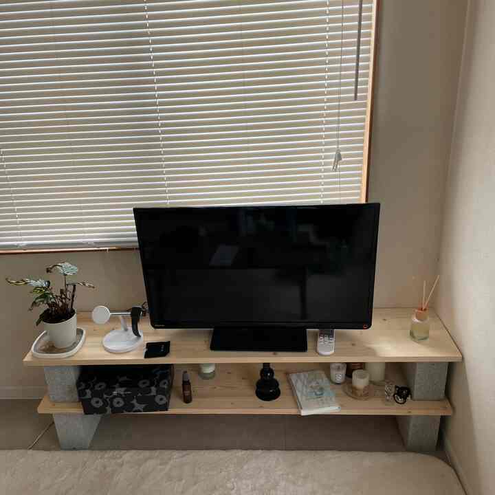 ベージュのブラインドと木目調のテレビ台があるシンプルなリビング、ディフューザーが飾られている