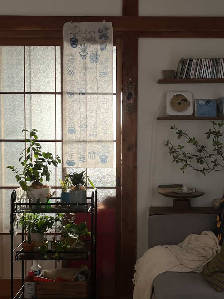 ナチュラルトーンの一人暮らしのリビング、ソファとキッチンワゴン、植物が配置された雰囲気のある空間