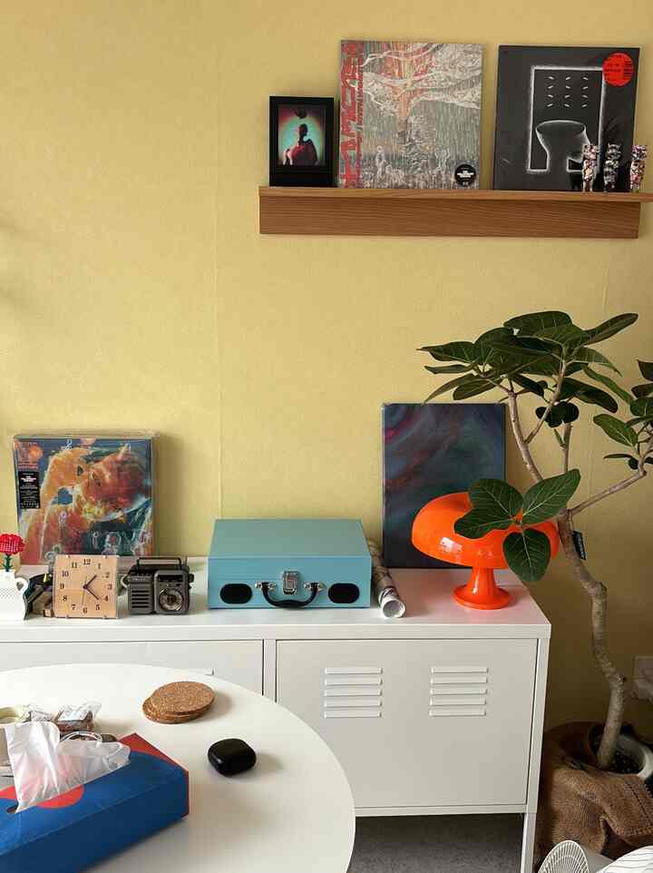 Natural style space with soft yellow walls and white cabinet, featuring a large plant and wooden shelf creating cozy atmosphere
