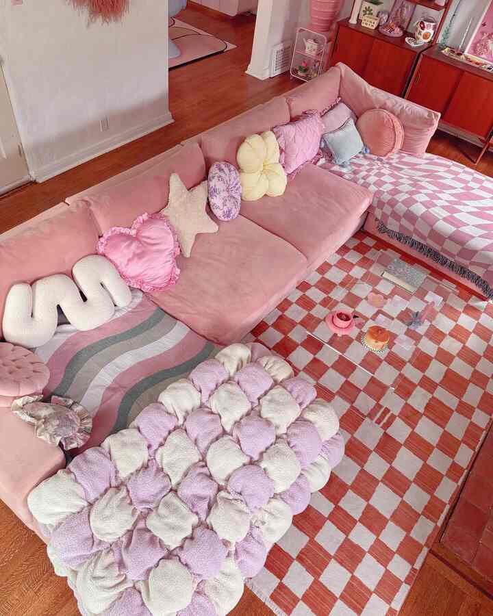 Warm pink-toned living room featuring a central pink sofa, checkered rug, and transparent coffee table, creating a cozy atmosphere
