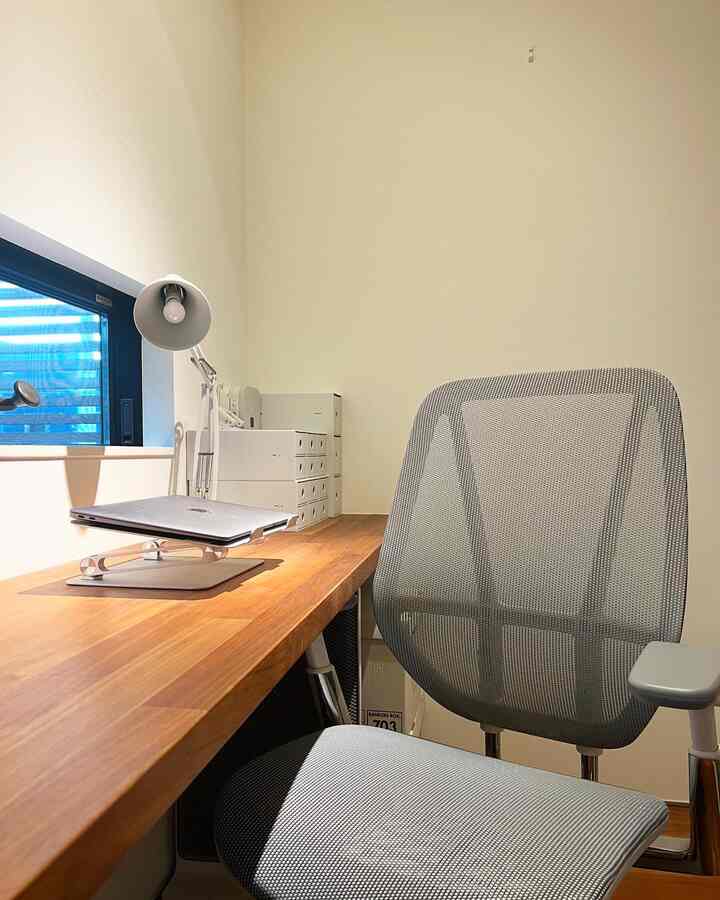 白い壁と木目調の机があるモダンな二人暮らしのホームオフィス、オフィスチェアとテーブルランプを備える雰囲気のあるインテリア