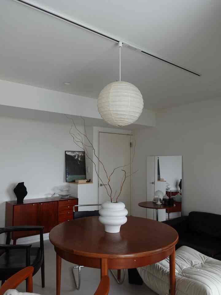 白い壁と天井、茶色の丸いダイニングテーブルに大きな白い花瓶が置かれたモダンなダイニングスペース