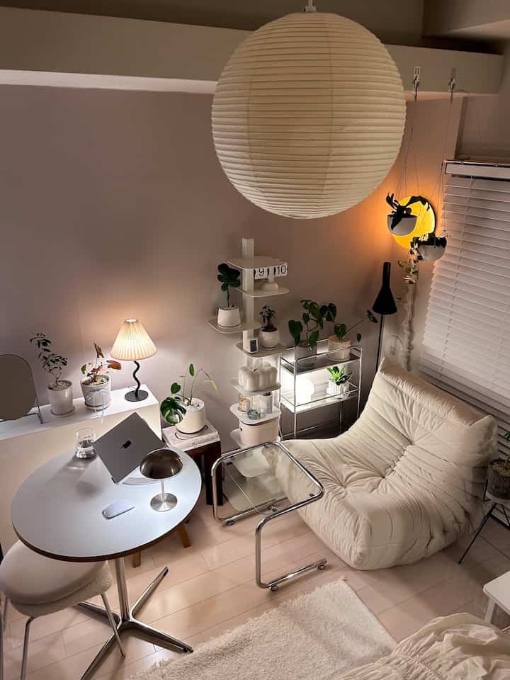 White and beige toned single-person living room with minimalist furniture and multiple plants creating a cozy atmosphere