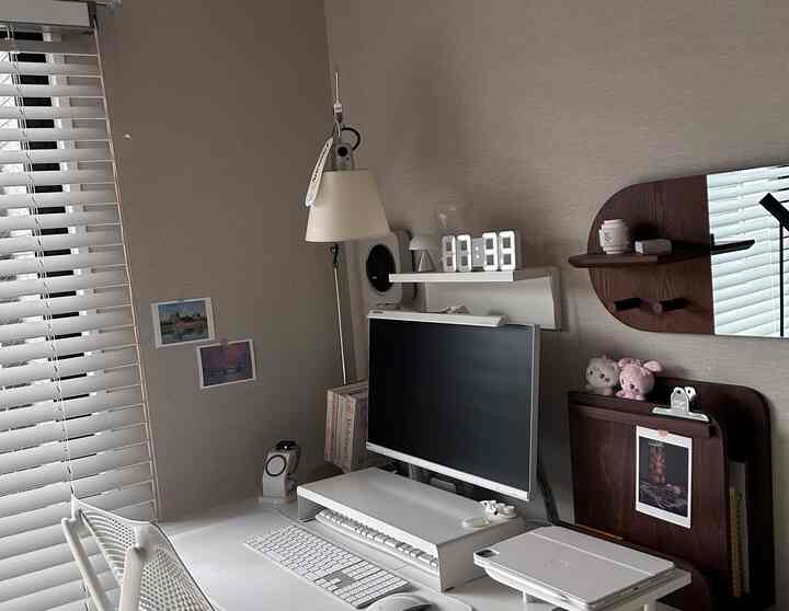 Modern white and beige home office featuring a compact desk, table lamp, wall mirror, and organized workspace with a calm ambiance