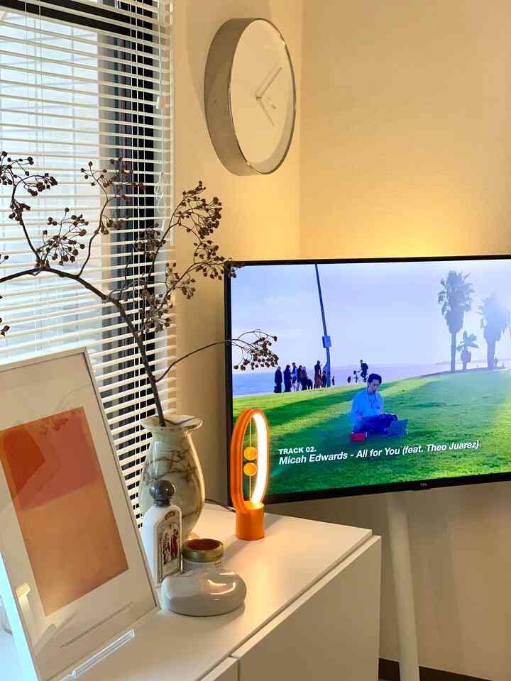 Warm beige toned living room featuring white TV stand with natural branch and orange lighting creating a cozy atmosphere