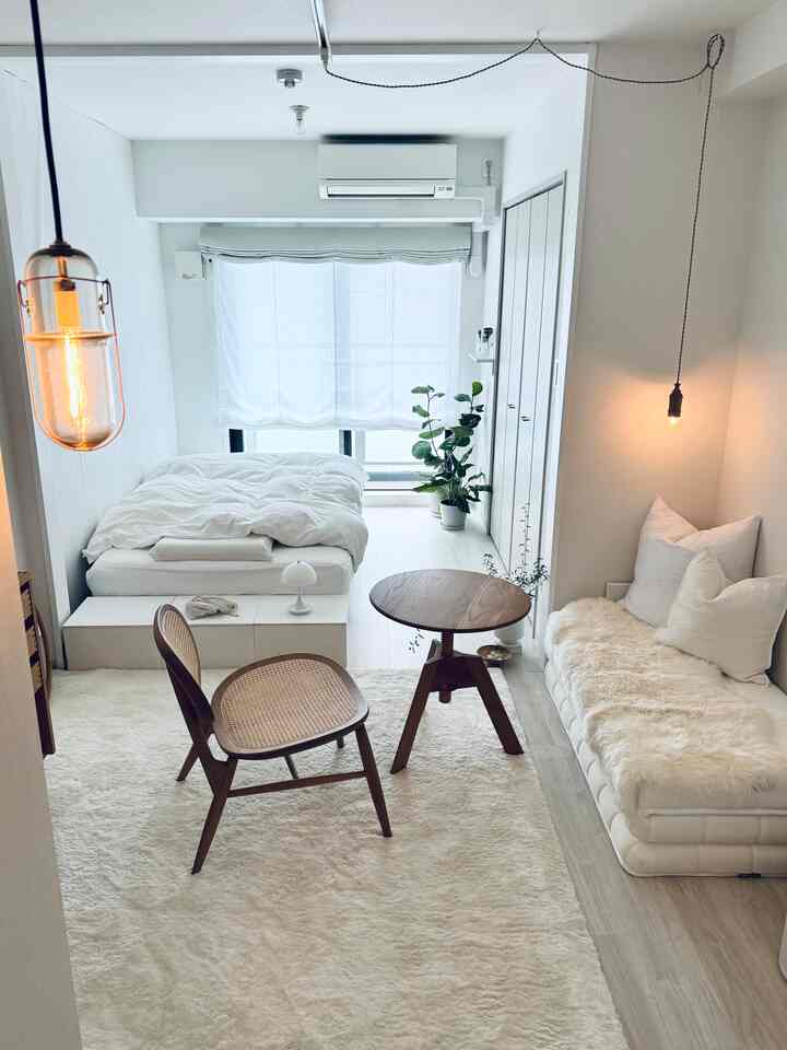 白を基調とした狭いリビング兼ベッドルーム、ナチュラルな木製家具と植物が配置されたミニマルなインテリア