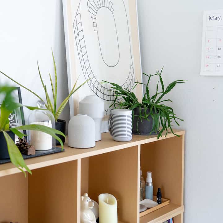 ベージュの収納棚が並ぶ空間に緑の植物とキャンドル、額縁が配置されたナチュラルモダンなインテリア