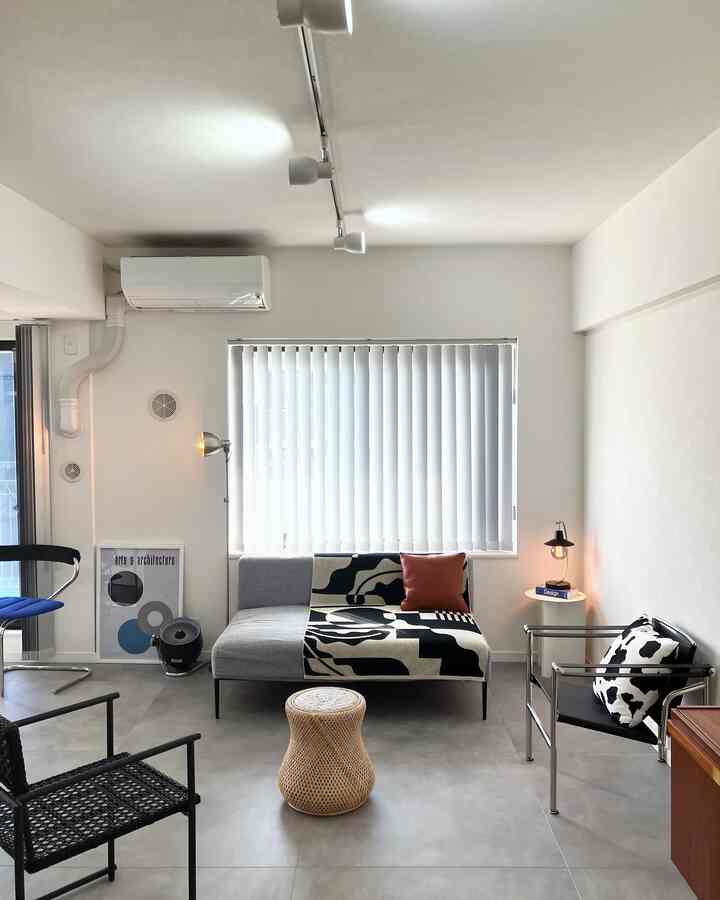 Simple living room in white and black tones featuring a gray sofa and rattan stool at center, with a modern atmosphere