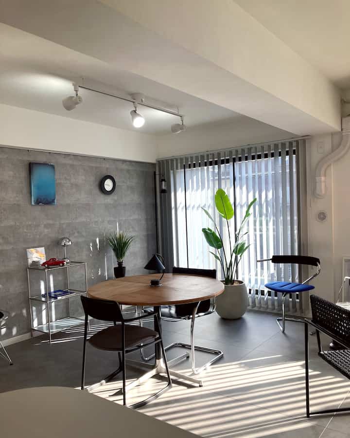 ナチュラルカラーとグレー調のダイニングルーム、丸テーブルと椅子、大きな観葉植物が配置された雰囲気のあるインテリア