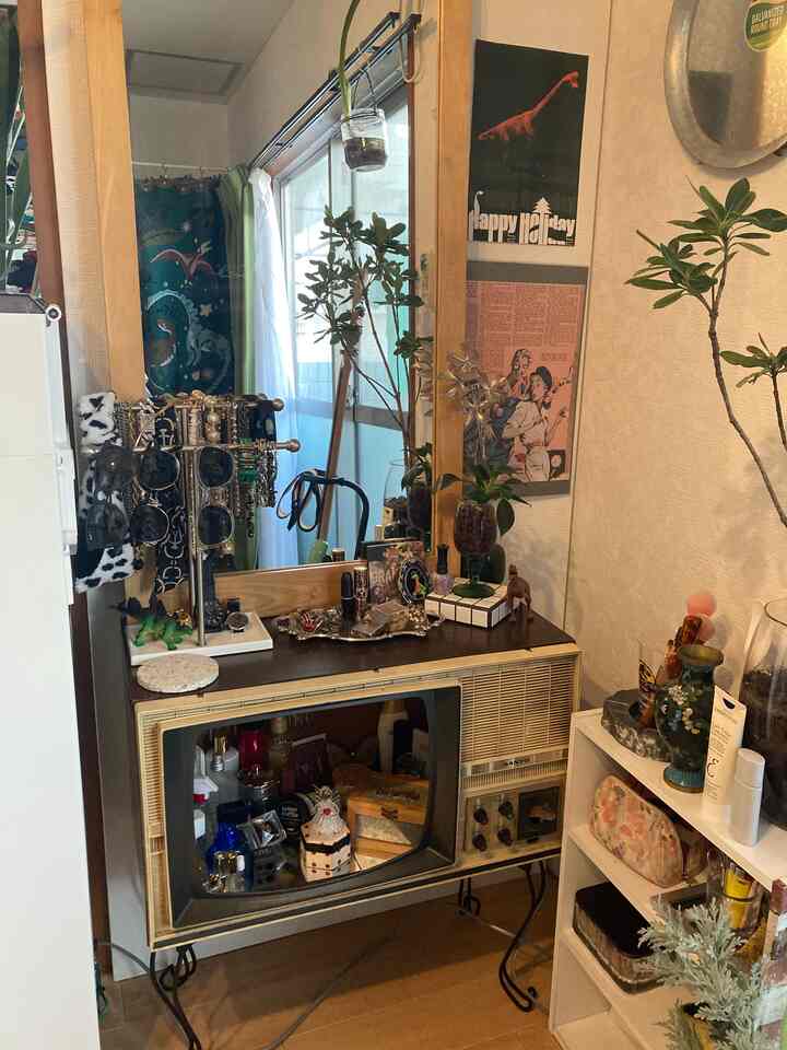 ナチュラルな色調の小さな部屋にレトロなテレビを化粧台として活用し、大きな鏡と装飾品が配置された雰囲気のあるインテリア
