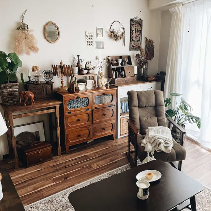 Natural brown toned living room featuring vintage wooden furniture, curtains, and plants creating a cozy atmosphere