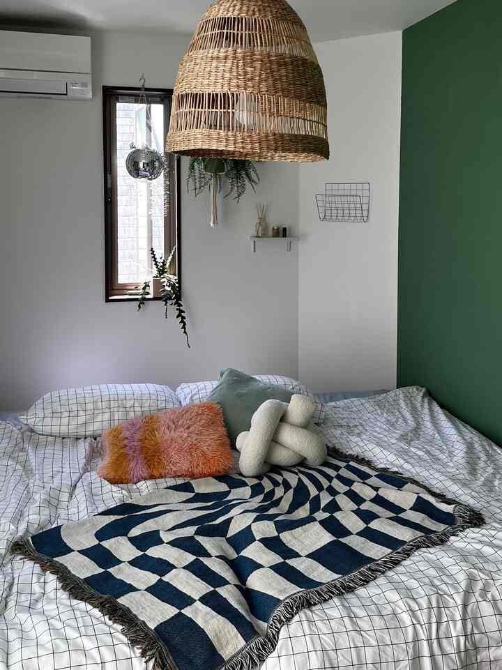 白と緑のトーンの寝室、チェック柄の寝具と複数のクッションが配置された自然で落ち着いた雰囲気のインテリア