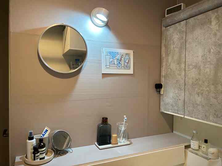 ベージュのトーンのバスルーム、丸い鏡とLEDブラケットライトが配置されたシンプルで整理された印象的な空間