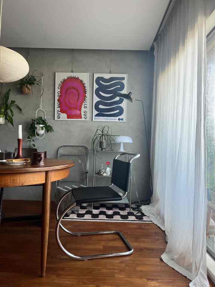 グレーのコンクリート壁と茶色の丸い木製ダイニングテーブル、黒いカンチレバーのダイニングチェアが配置されたミッドセンチュリーモダン風の北欧ダイニングルーム