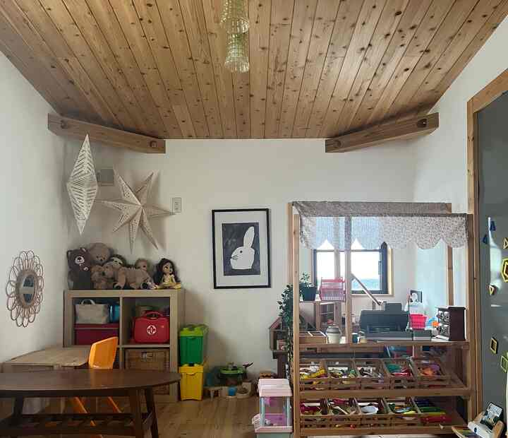ナチュラルな色調の子供部屋、木の天井と床、玩具収納と遊び場が配置された雰囲気の良い空間