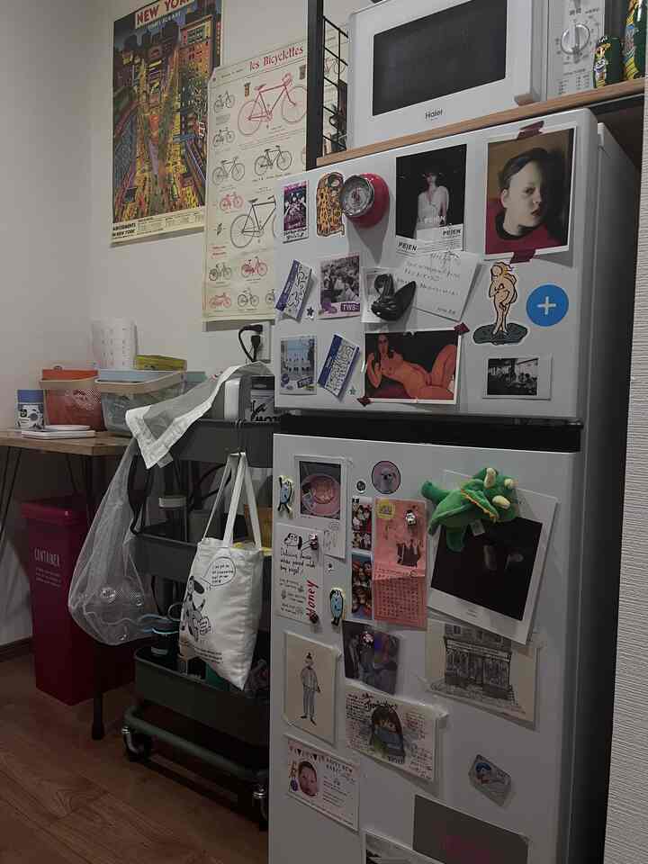 ブラウンの木製床と白い家電が配置されたキッチン、キッチンワゴンとポスターで飾られた雰囲気のある空間