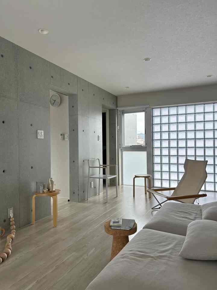 Natural modern living room featuring gray concrete walls, white sofa, and natural wood stools on light wood flooring