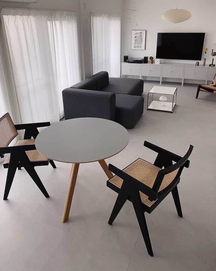 白とグレーのトーンでまとめられたシンプルモダンなリビング、グレーのソファと丸テーブル、黒い椅子が配置された印象的な空間