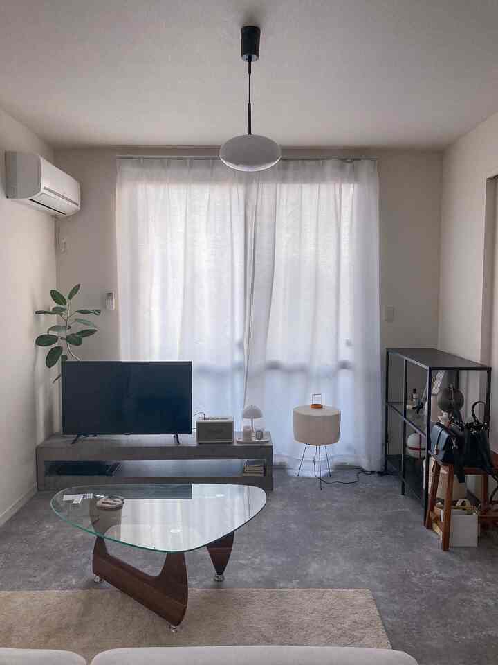 モノトーンと白の色調の一人暮らし用リビング、シンプルで整ったテレビ台とガラスのコーヒーテーブルが配置された印象的な空間