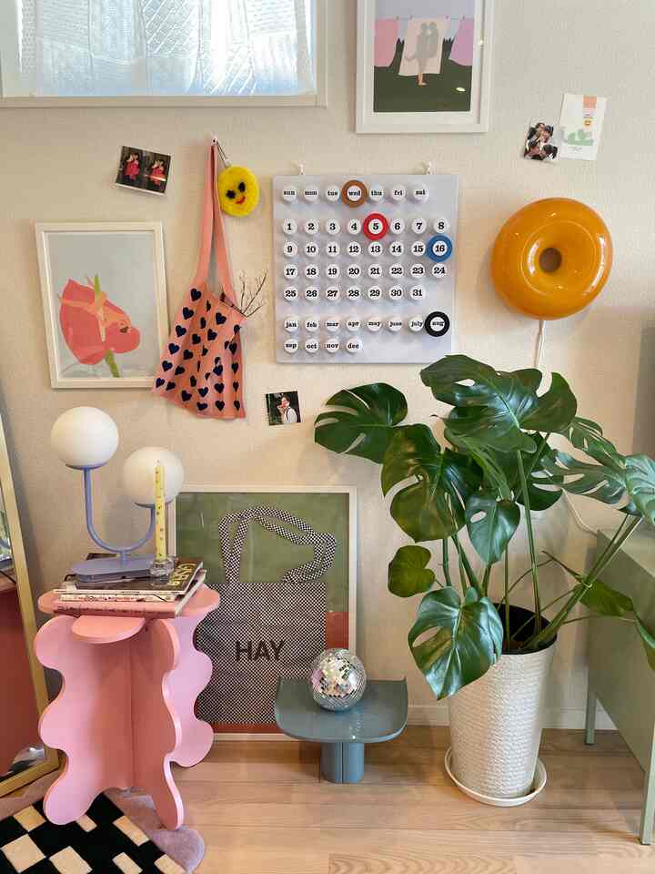 Natural wood floor space featuring large green plant, pink side table, and soft lighting with cozy decorated wall