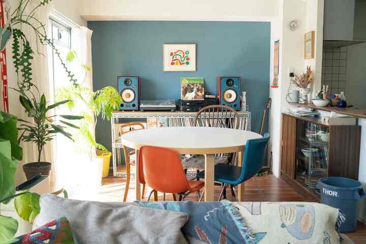 青い壁が印象的なダイニング、丸テーブルとカラフルな椅子が配置された自然な雰囲気の空間