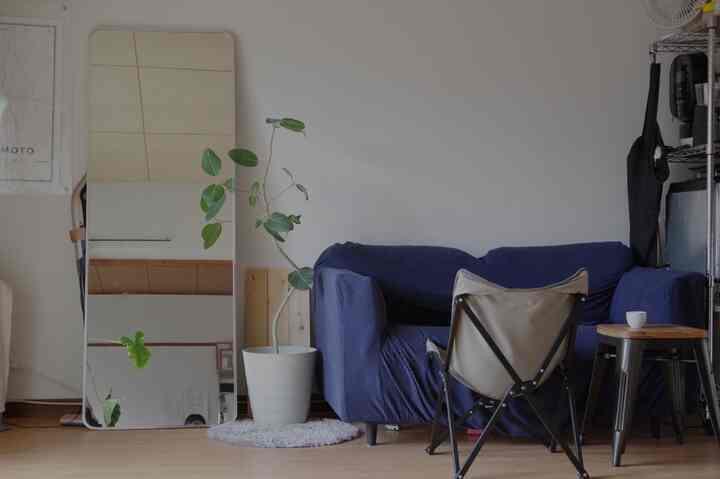 White-walled living room with blue sofa, stool, and a standing mirror creating a cozy single household space