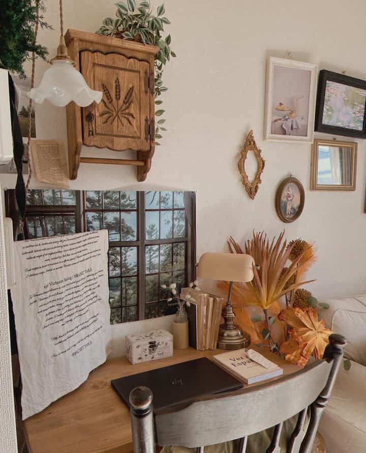 柔らかなナチュラルトーンのリビングルーム、木製デスクとソファ、ポスター、ブラケットライトが配された雰囲気のあるインテリア