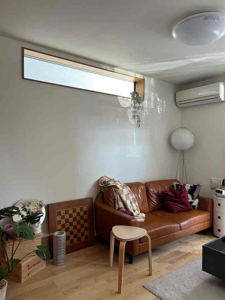 A living room with white walls and wood tones flooring, featuring a brown leather sofa and floor lamp in a simple natural setting