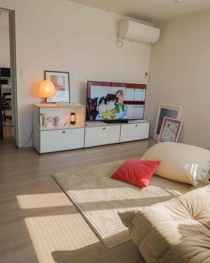 明るいベージュとホワイトのトーンのリビング、ビーンバッグソファとテレビ台、落ち着いた照明が調和したシンプルなインテリア