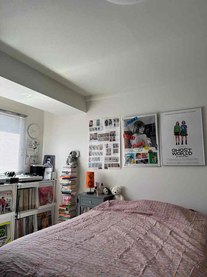 White-toned bedroom featuring bed, bookshelf, and wall posters creating a cozy space