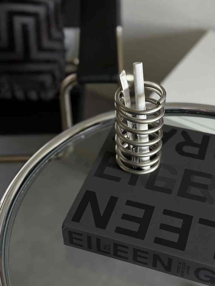 黒とシルバーのトーンが特徴的なホームオフィス空間、ガラステーブルにステンレススチールの小物と本が置かれたミニマルなインテリア